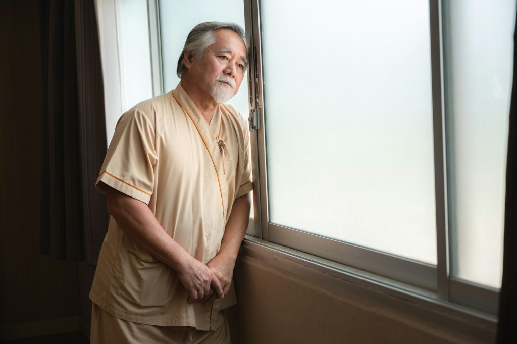 Old man standing beside a window